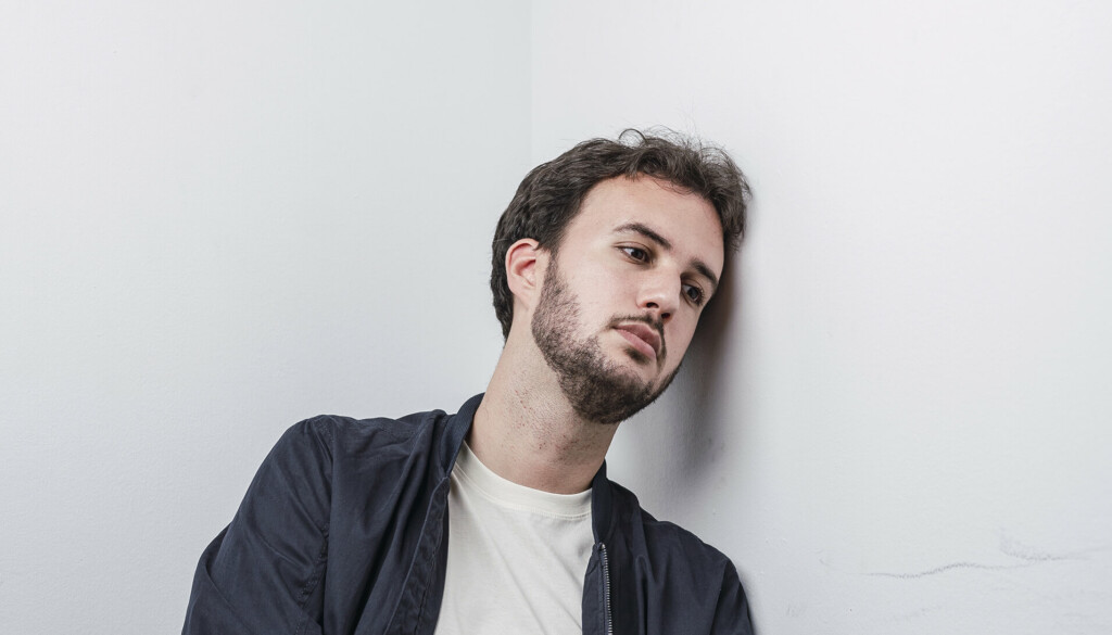 Young man with a blank expression leaning against a wall.