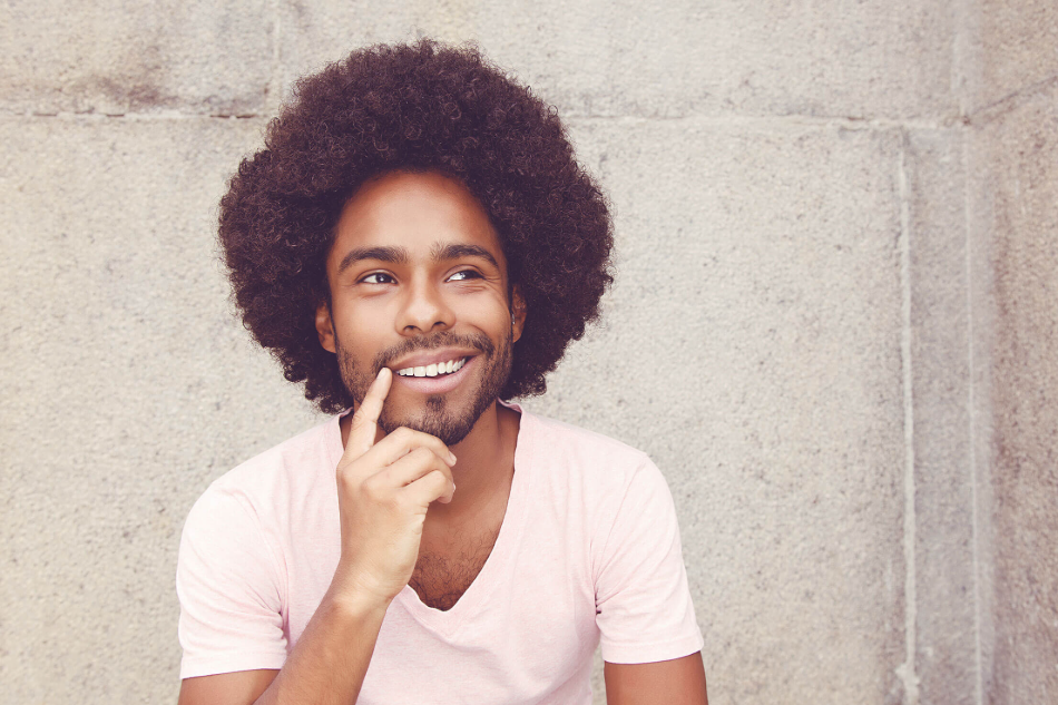 Man with voluminous curly hair smiling while touching his face, showcasing healthy hair growth.