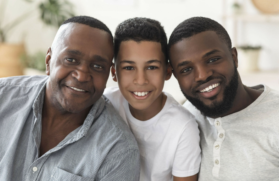 Three generations of men smiling together, illustrating how male pattern baldness can affect different ages.