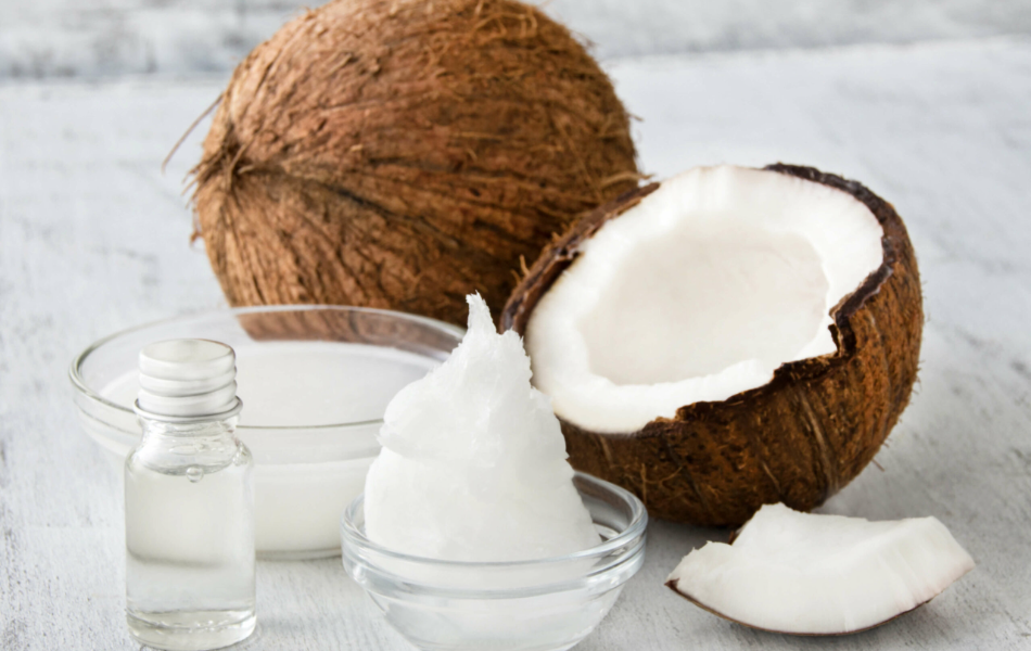 Glass bowls and bottles filled with different types of coconut oil, next to a halved and whole coconut.