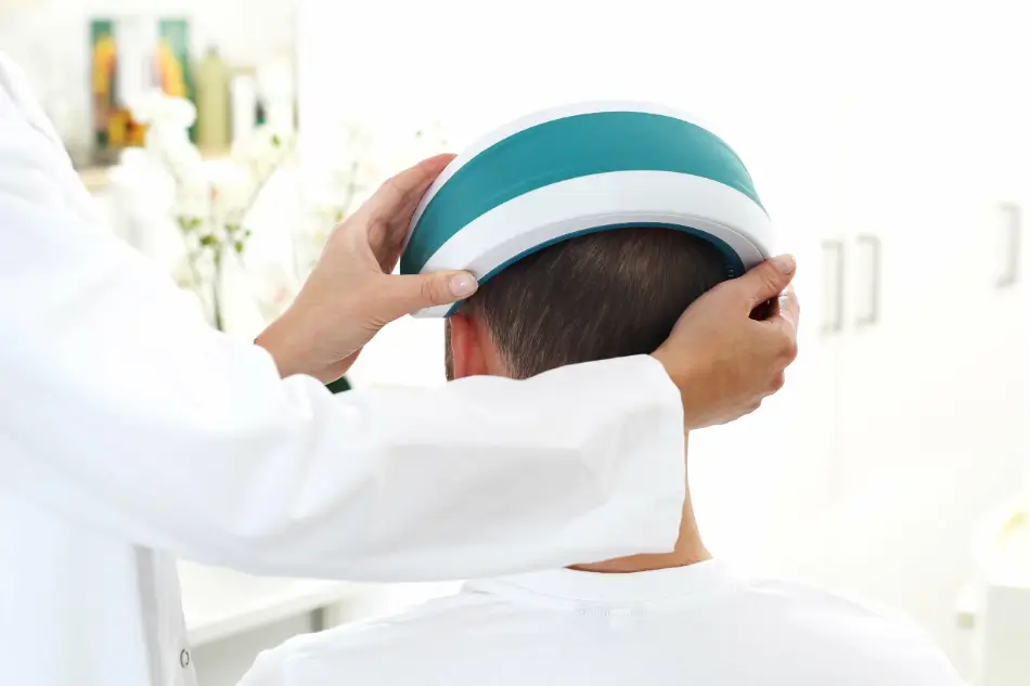 Doctor placing an LLLT helmet on a patient's head for hair regrowth treatment.